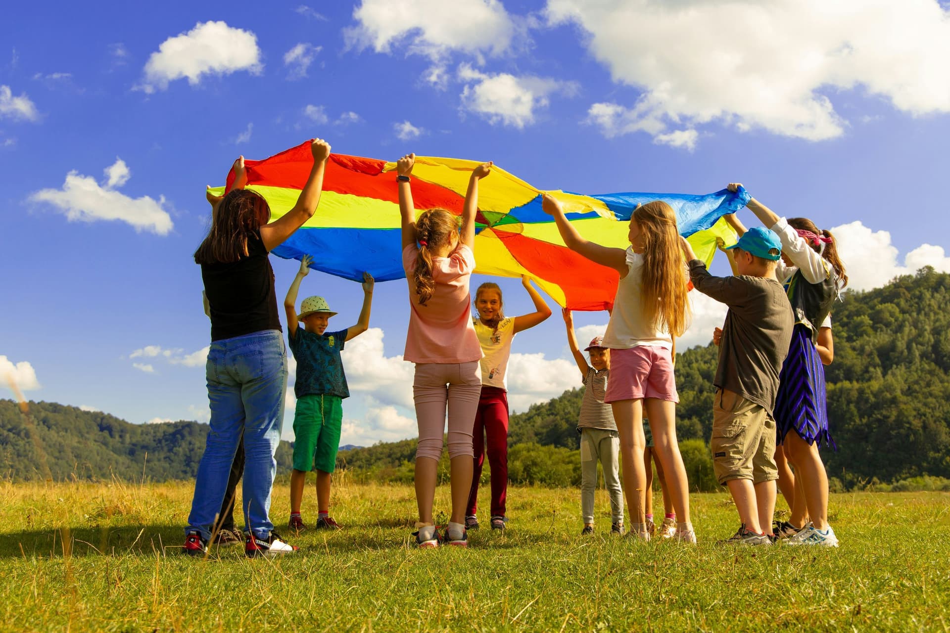 Groep kinderen speelt samen buiten met een kleurrijke parachute — inclusief spelen mogelijk gemaakt door Stichting Edith Devriendt
